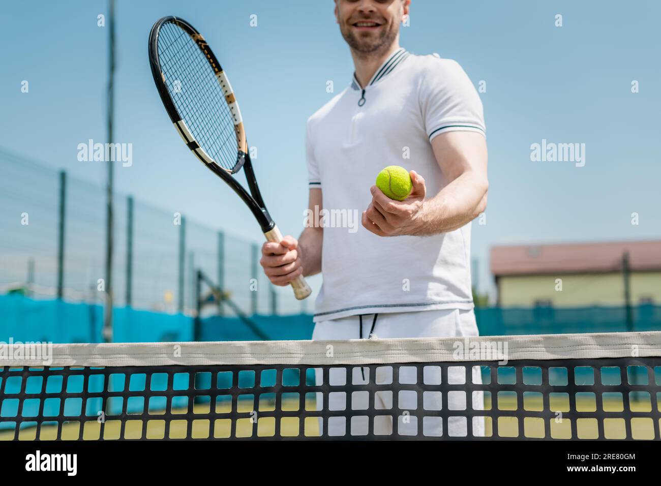 vista ritagliata dell'uomo in abbigliamento sportivo con racchetta da tennis e palla vicino a rete, giocatore, hobby e sport Foto Stock