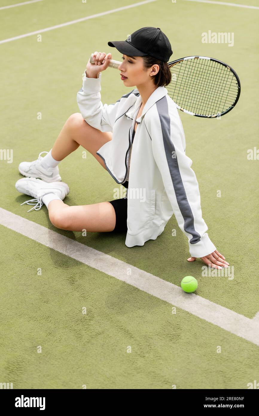 donna con abbigliamento sportivo e berretto seduto sul campo da tennis,  palla e racchetta, tennista femminile, sport Foto stock - Alamy