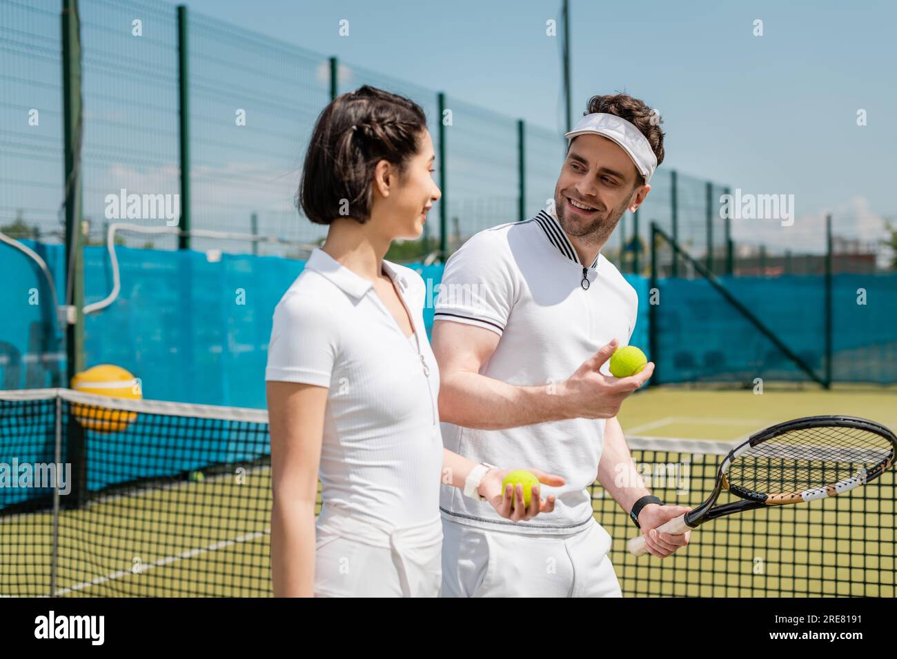 uomo e donna positivi che tengono palle da tennis e racchetta in campo, hobby e tempo libero Foto Stock