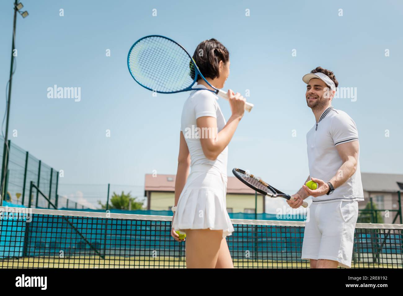 coppia positiva che tiene palle da tennis e racchette sul campo, hobby e tempo libero estivo, sport Foto Stock