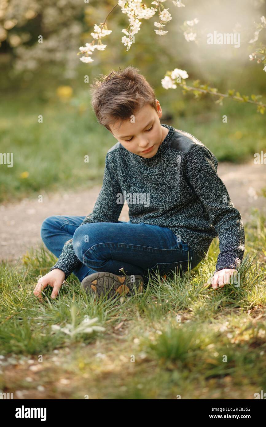 Il ragazzo è seduto sull'erba nel giardino in fiore. Foto Stock