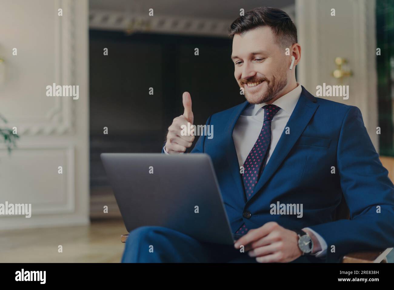 Un professionista professionale felice in un elegante abito, che mostra soddisfazione con un gesto del pollice durante una videoconferenza con il capo o i colleghi su un lapt Foto Stock