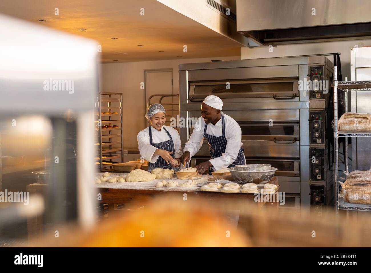 Allegri fornai diversi che indossano grembiuli nella cucina del panificio e tagliano l'impasto Foto Stock