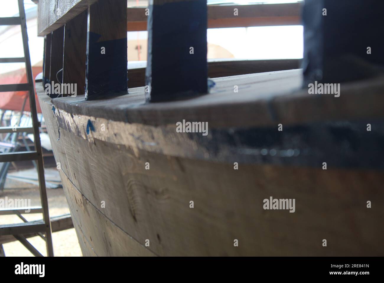 Un primo piano del lato di una barca di legno in costruzione con una scala sullo sfondo. Foto Stock