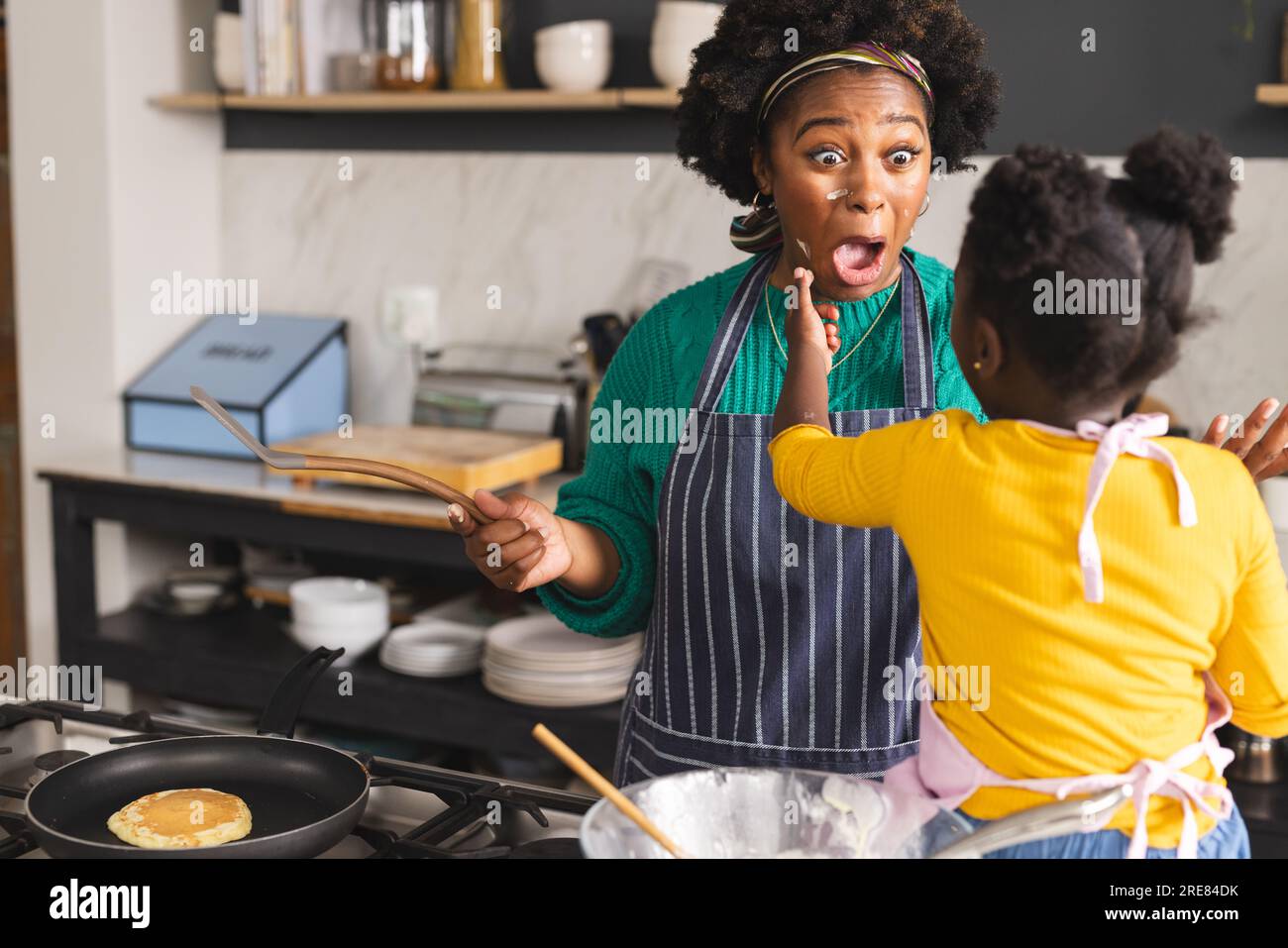 La madre e la figlia afro-americana allegri preparano pancake in cucina a casa Foto Stock