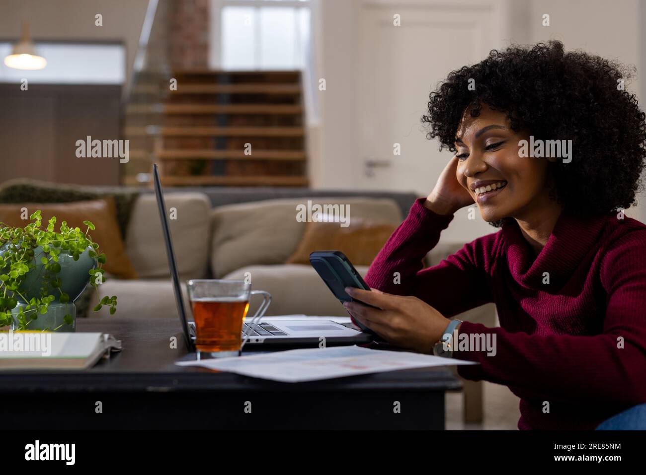 Donna birazziale felice che usa il computer portatile e lo smartphone a casa Foto Stock
