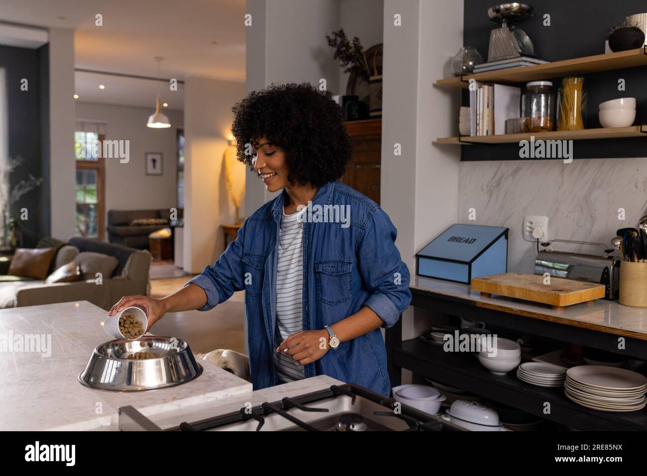 Felice donna birazziale che serve cibo per cani in cucina Foto Stock