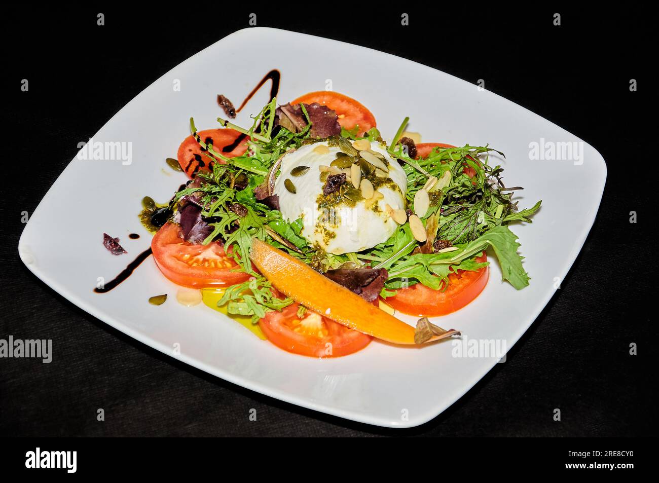 Insalata di burrata in piatto bianco su sfondo nero Foto Stock