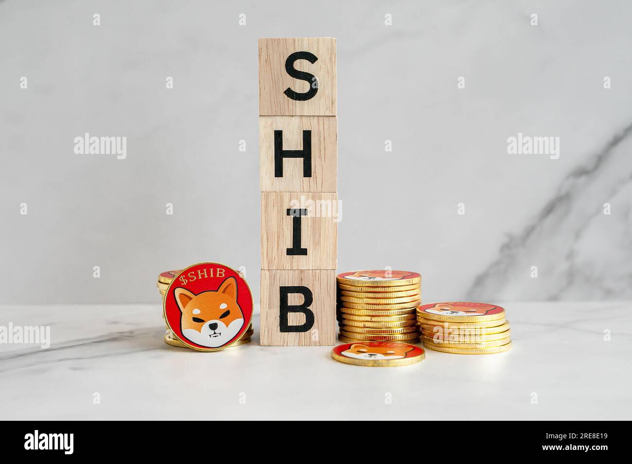 Molte delle monete Shiba inu (SHIB) sono collocate verticalmente accanto a un blocco di legno al centro con uno sfondo di marmo bianco. Foto Stock