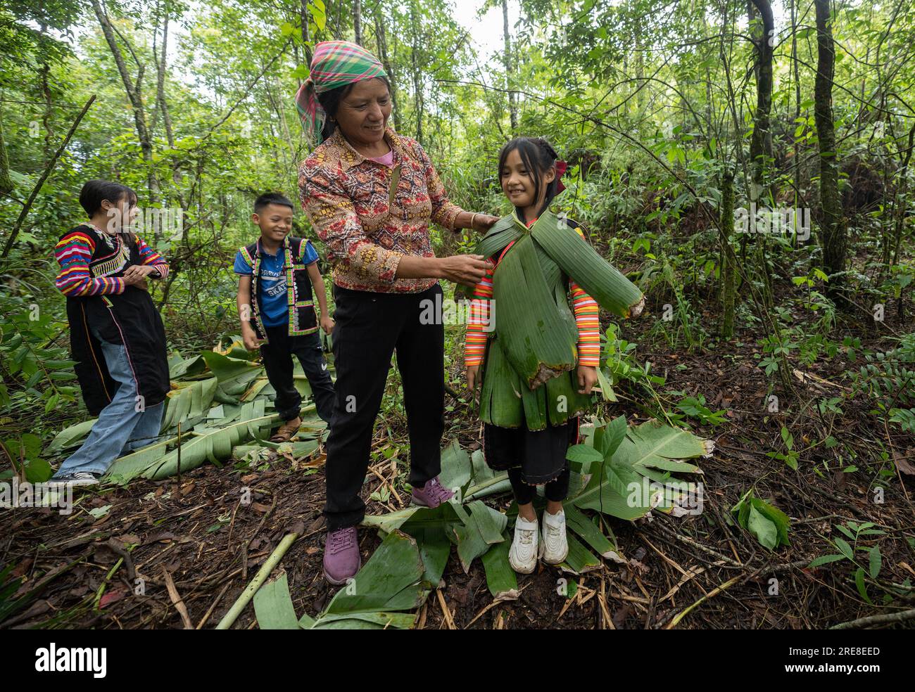 (230726) - JINPING, 26 luglio 2023 (Xinhua) - la moglie di Zhang Puzhong Wang Suying (2nd R) veste sua nipote con foglie di banana nella foresta vicino al villaggio di Xiaxinzhai, Zhemi Township, Jinping County, Honghe Hani e Yi, provincia dello Yunnan della Cina sud-occidentale, 23 luglio 2023. Dopo giorni di riflessione, Zhang Puzhong decise di fare qualcosa di istruttivo ai suoi nipoti: Riportarli nella foresta che abitava da bambino più di 60 anni fa. E' molto importante. So quanto sono felice oggi perché non dimentico mai quanto fosse amara la mia vita in passato", ha detto Zhang. Foto Stock