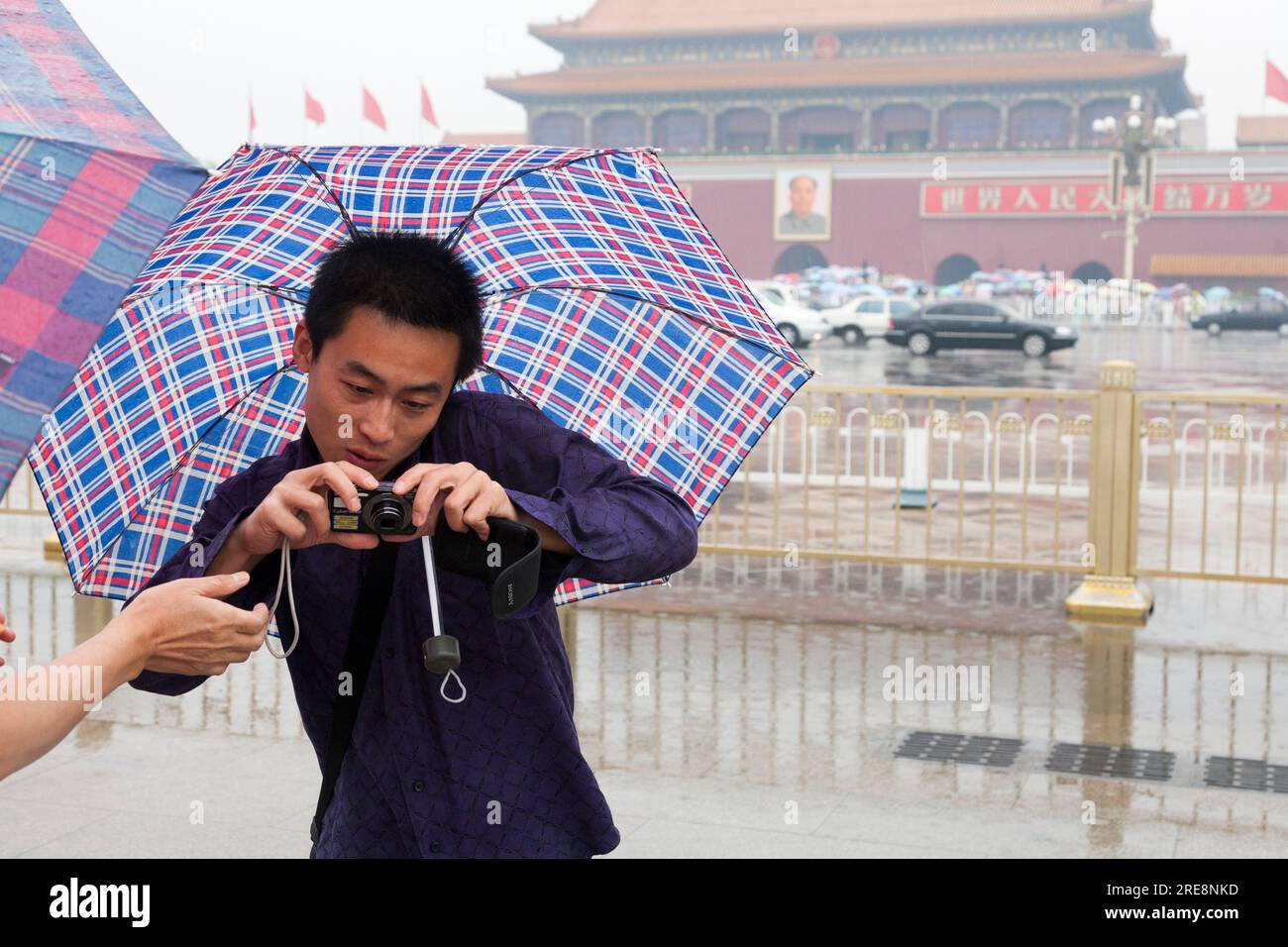 Fotografo turistico cinese che si protegge dalla pioggia con un ombrello mentre scatta una foto con una fotocamera digitale in una giornata umida in Piazza Tiananmen, Pechino, Cina. Ritratto del Presidente Mao TSE Tung orologi dalle mura della città Proibita. (125) Foto Stock