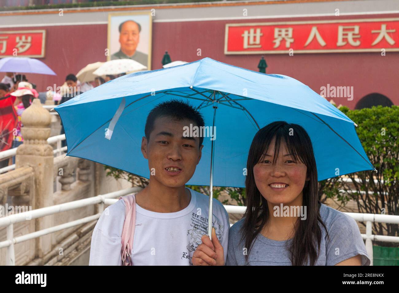 Coppia turistica cinese che si protegge dalla pioggia con ombrelloni in una giornata umida in Piazza Tienanmen, Pechino, Cina. Ritratto del Presidente Mao TSE Tung orologi dalle mura della città Proibita. (125) Foto Stock