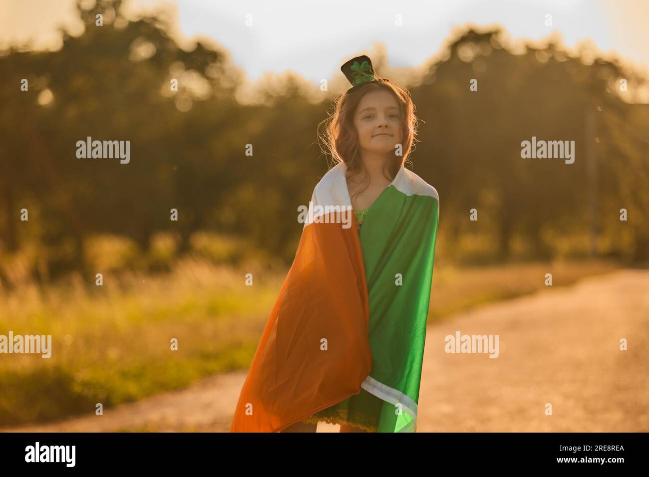 Adorabile ragazza leprecaun coperta di grande bandiera irlandese durante la celebrazione del giorno di San Patrizio Foto Stock