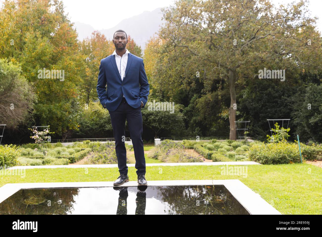 Premuroso sposo afroamericano in piedi accanto al laghetto nel giardino soleggiato, spazio fotocopie Foto Stock