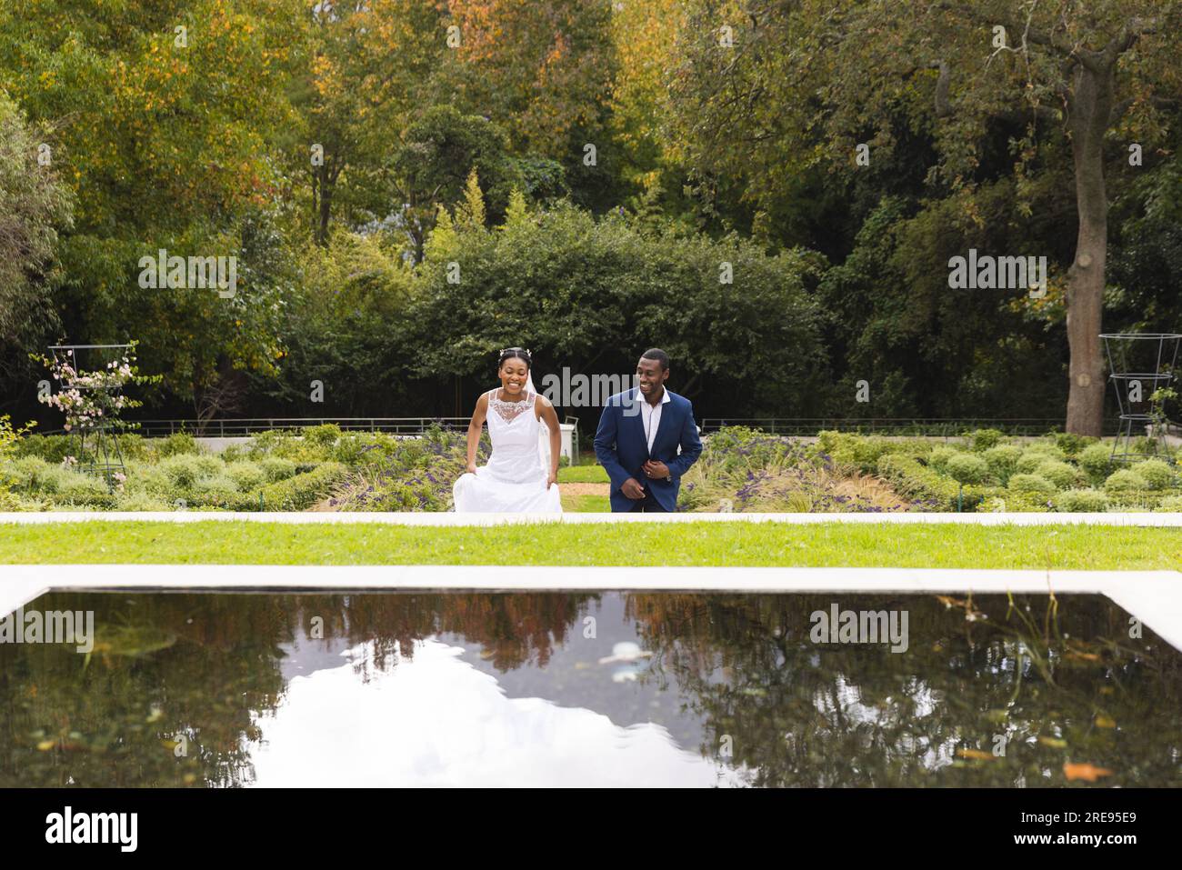 Felice sposo e sposo afroamericano il giorno del matrimonio passeggiando insieme in giardino, spazio fotocopie Foto Stock