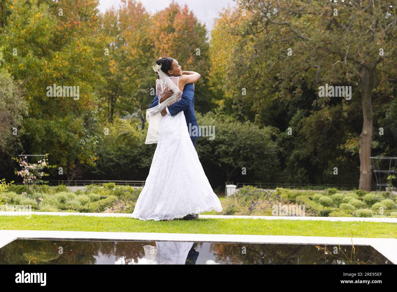 Felice sposo e sposo afro-americano che abbraccia il giorno del matrimonio nel soleggiato giardino, spazio fotocopie Foto Stock
