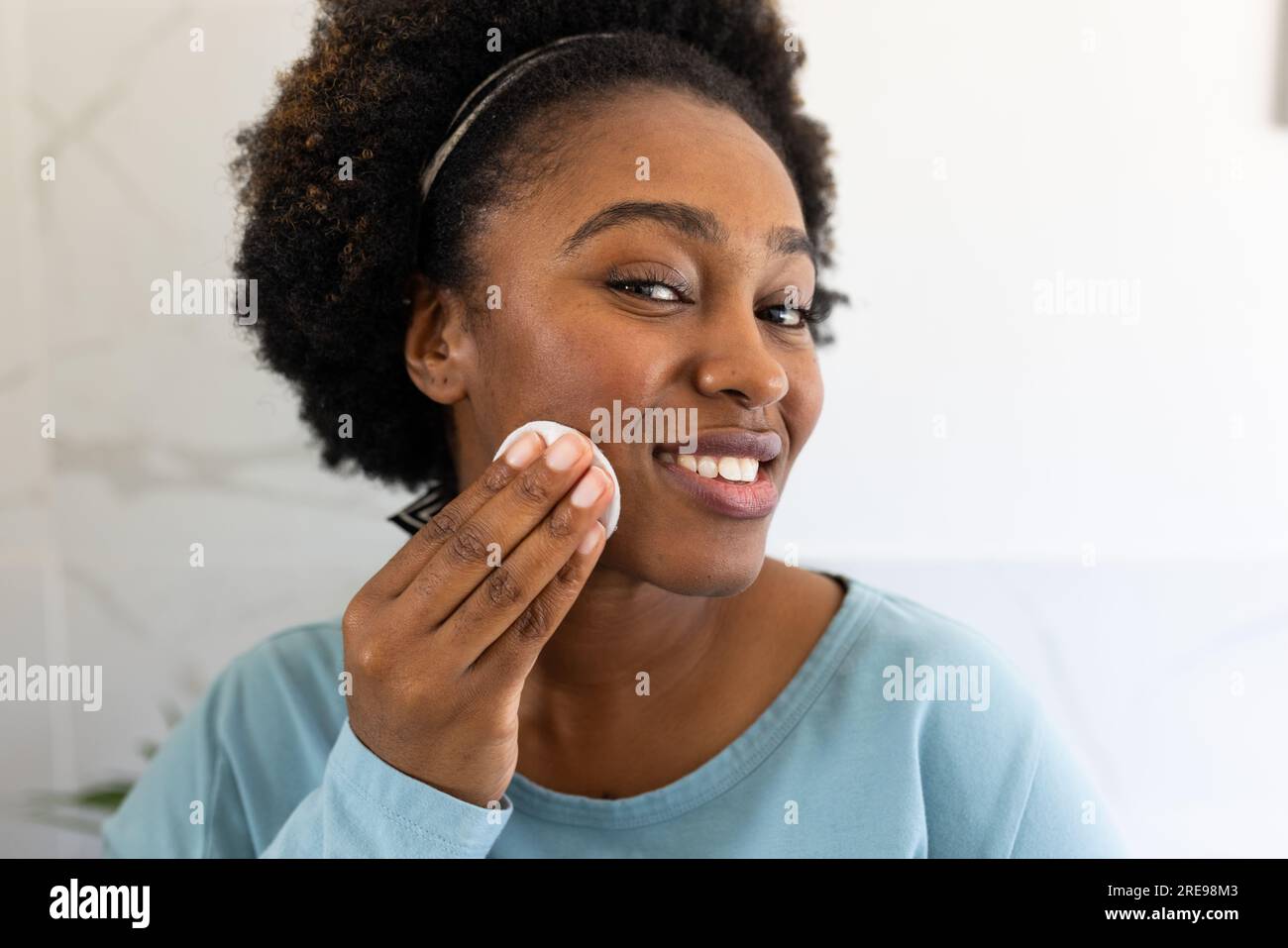 Donna afro-americana felice più grande che applica polvere sul viso in bagno Foto Stock