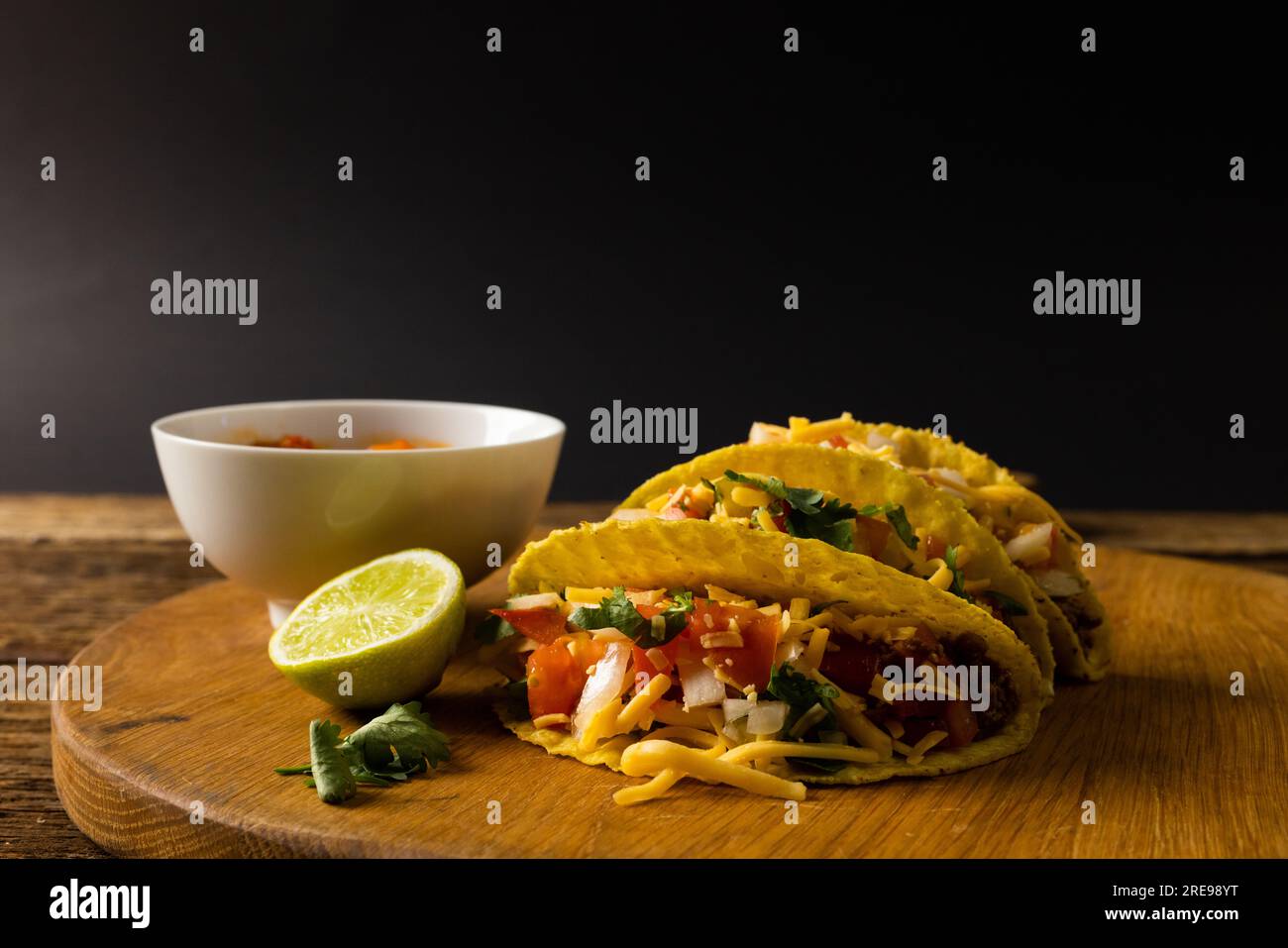 Primo piano di tacos con fetta di limone, coriandolo e ciotola su tavola da portata su sfondo nero Foto Stock