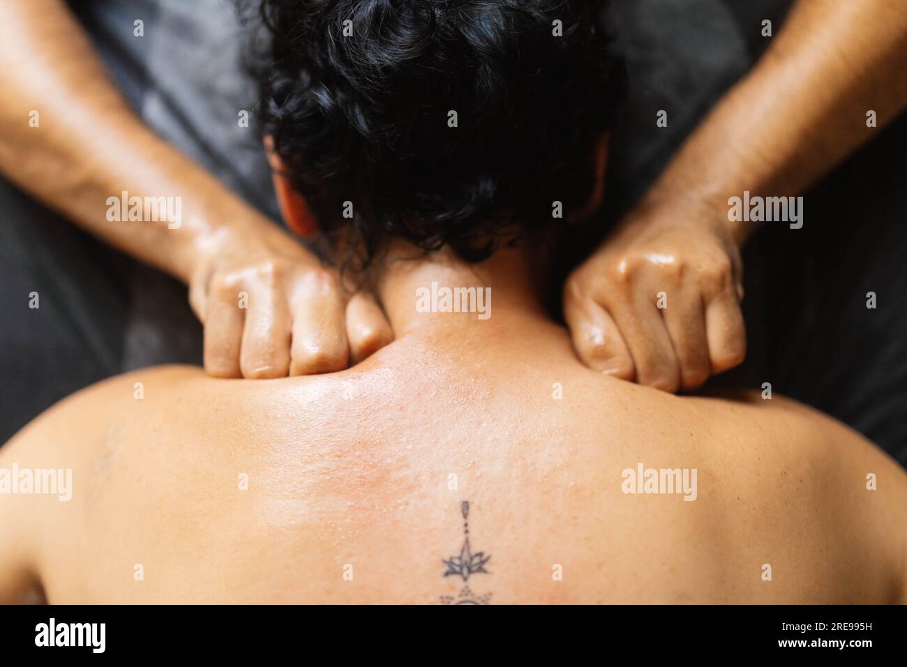 Terapista maschile irriconoscibile mentre si è in piedi alla scrivania e si sta impastando le spalle con le dita piegate su una cliente femminile anonima Foto Stock