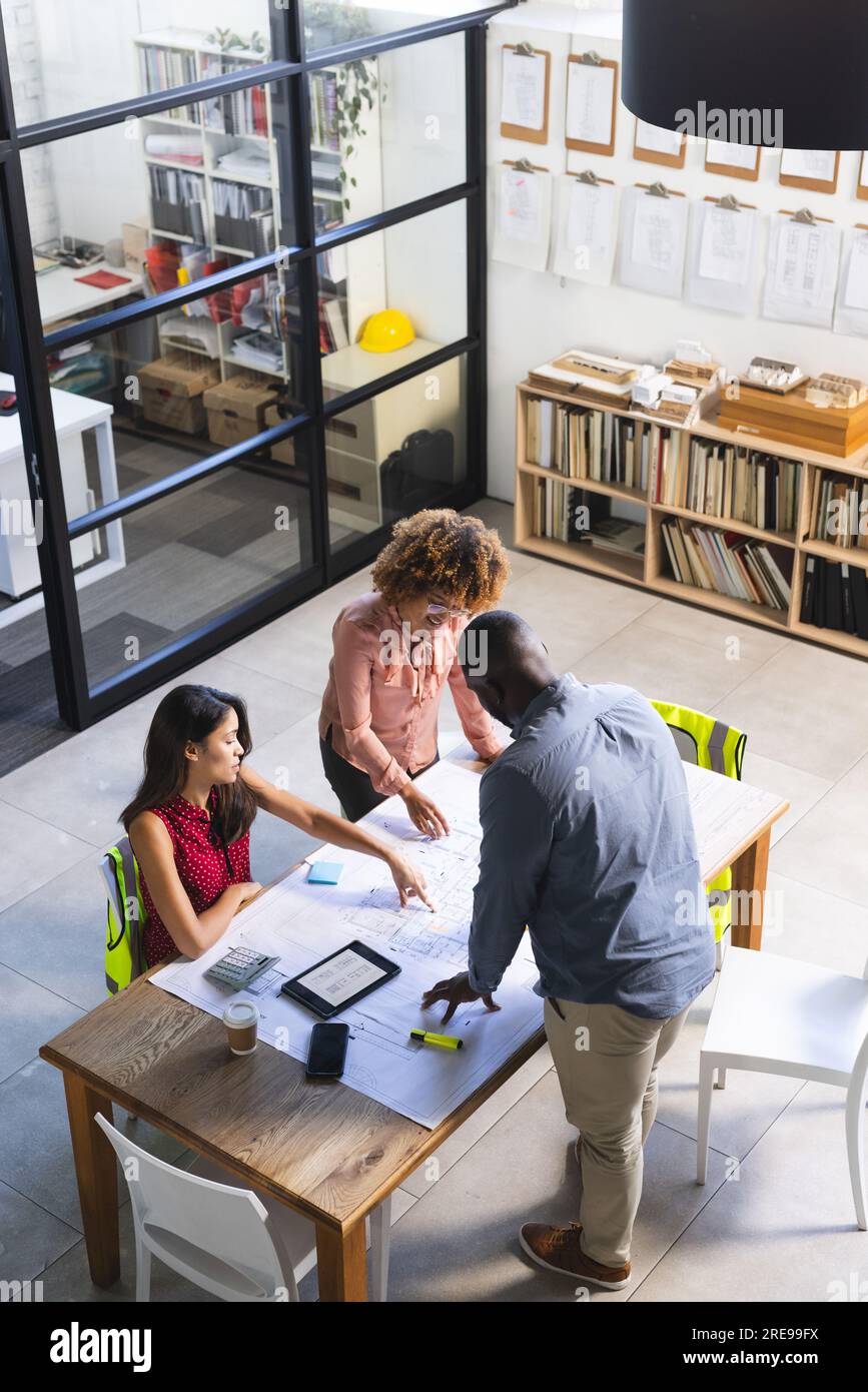 Felice e diversificato colleghi che discutono di lavoro con il tablet rispetto al progetto di costruzione in ufficio Foto Stock