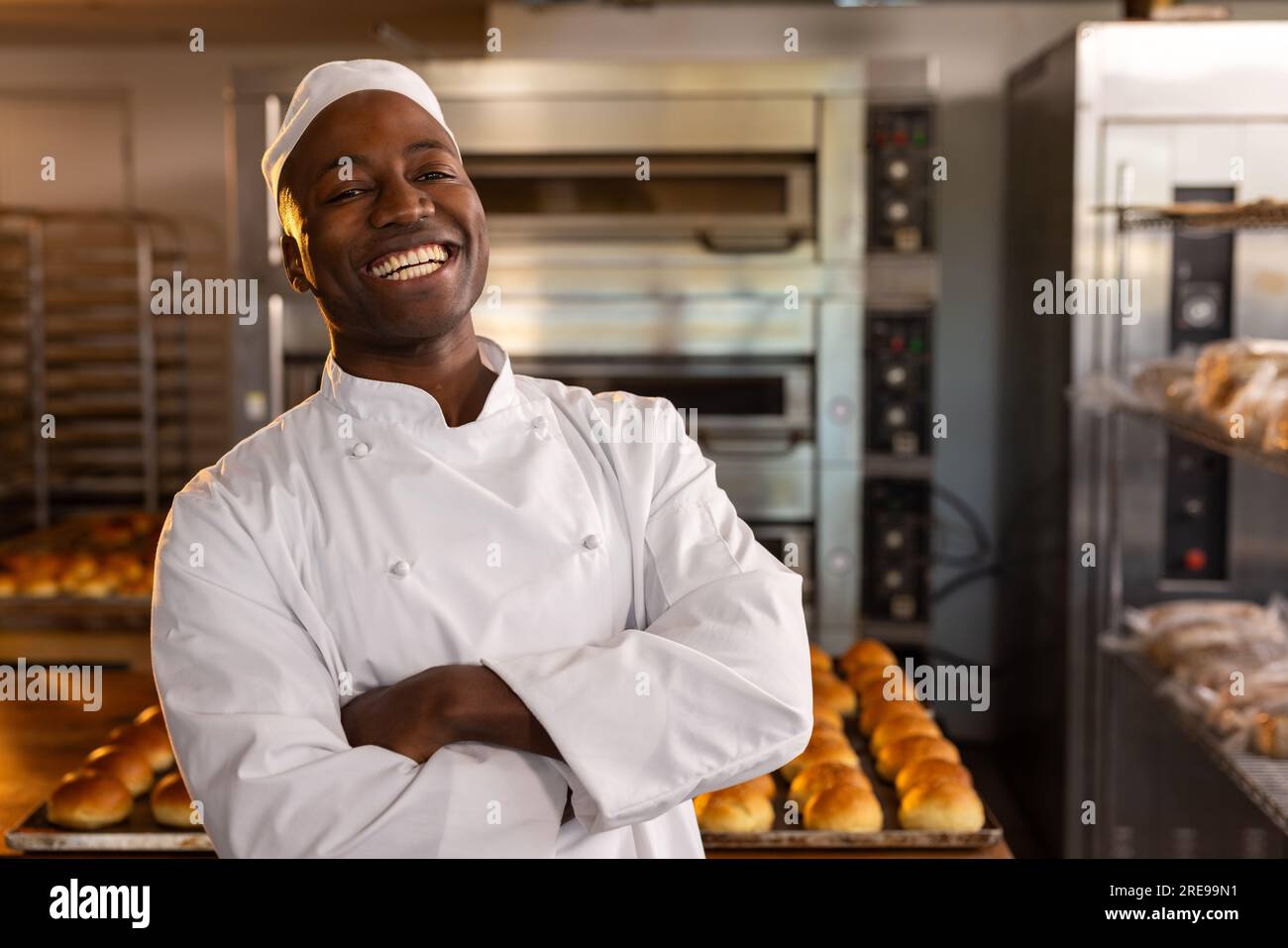 Ritratto del fornaio afro-americano con le braccia incrociate nella cucina del forno su panini freschi Foto Stock