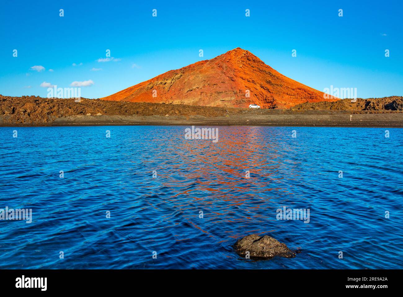 Un vulcano rosso riflesso nelle acque blu di playa de Janubio a Lanzarote Foto Stock