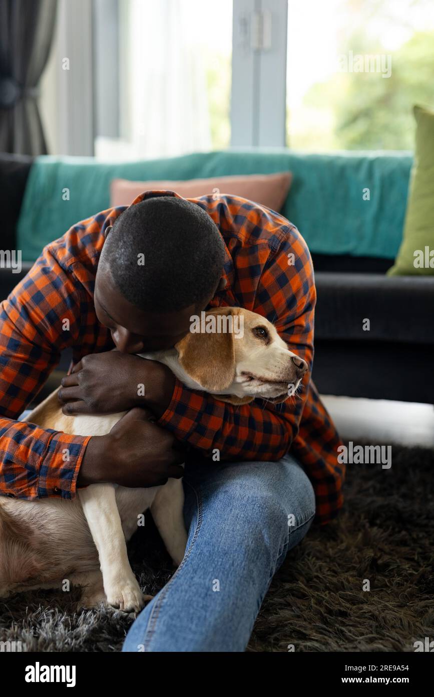 Felice afro-americano seduto sul pavimento ad abbracciare i suoi cani da compagnia a casa Foto Stock