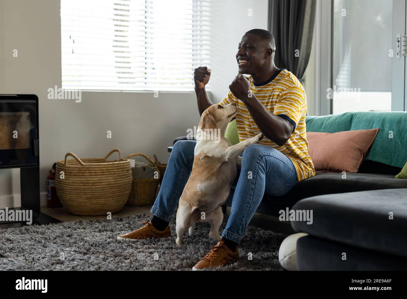 Uomo afro-americano che guarda la partita di rugby e sostiene, con il suo cane domestico a casa Foto Stock
