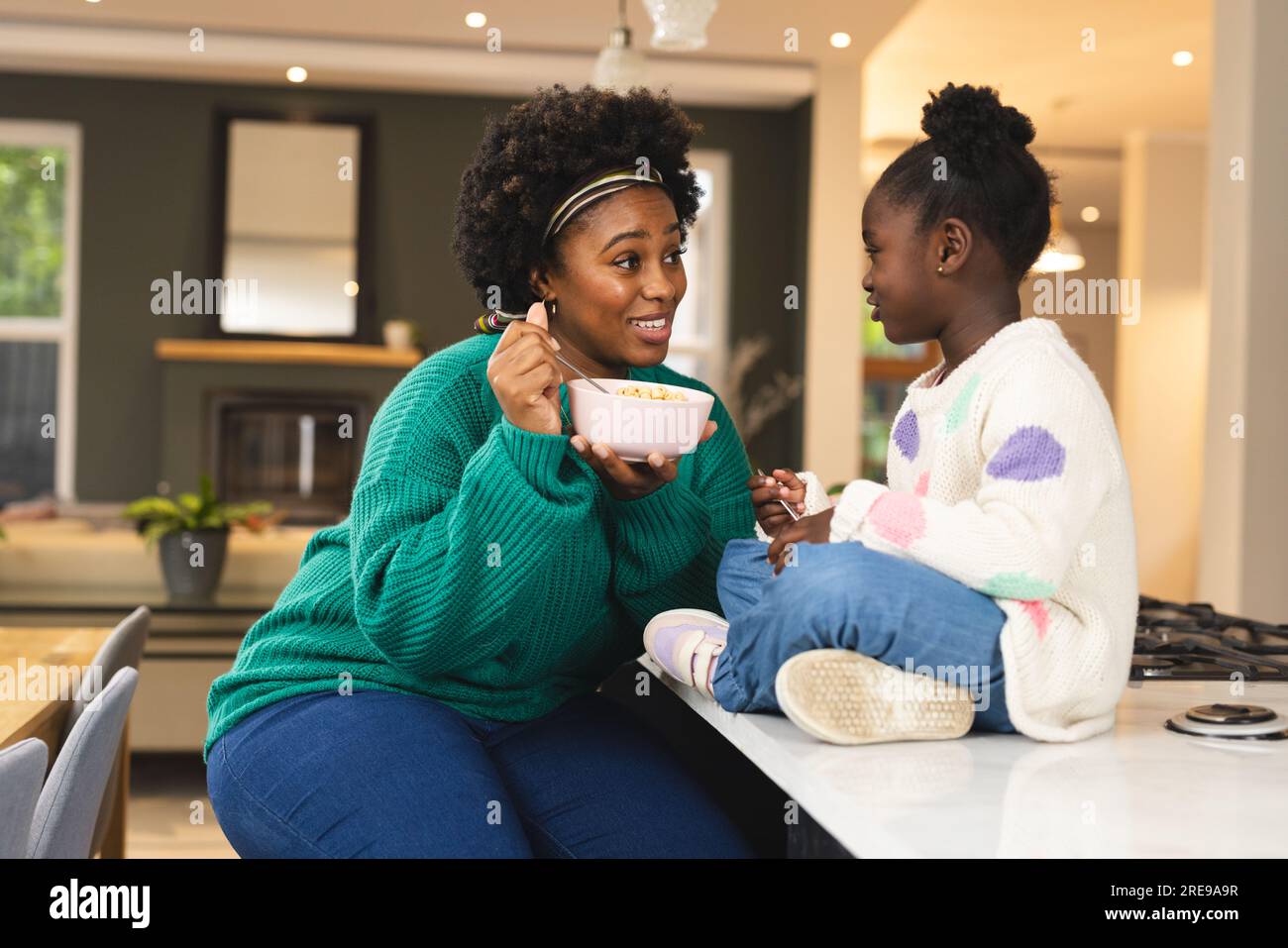 La madre e la figlia afro-americane felici sedute sul piano di lavoro a colazione a casa Foto Stock