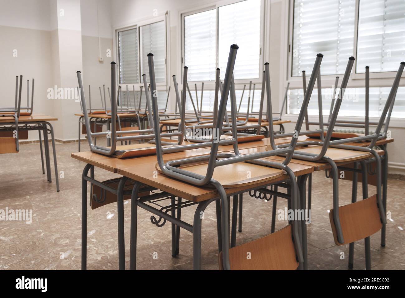 Primo piano di sedie simili capovolte posizionate su un tavolo di legno in classe leggera dopo le lezioni Foto Stock