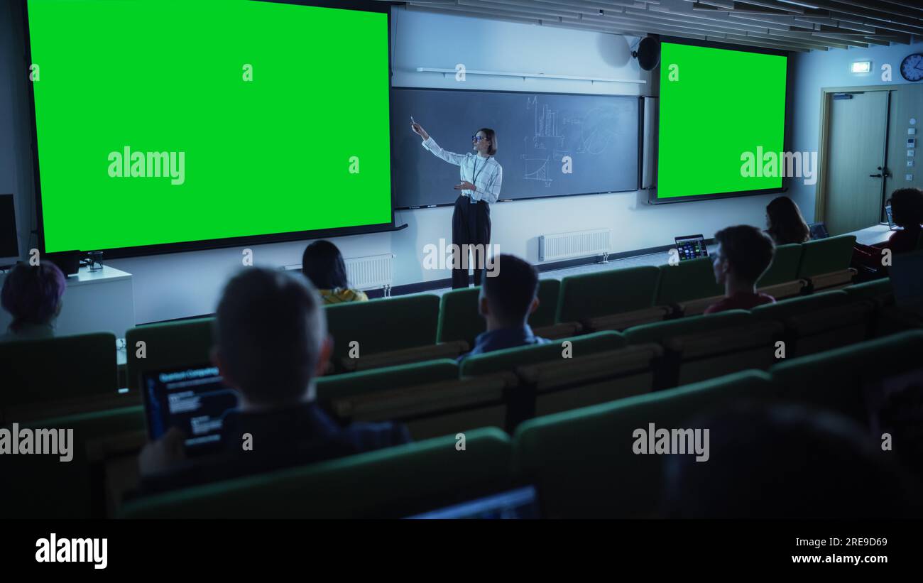 Giovane professoressa universitaria donna che spiega una lezione, puntando su una schermata verde fittizia. Gruppo di diversi studenti multietnici Foto Stock
