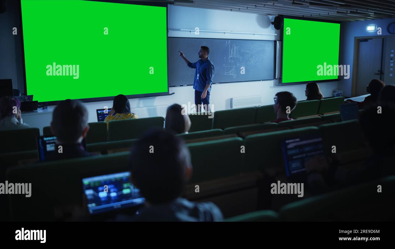 Giovane professore universitario che spiega una lezione, puntando su una schermata verde fittizia. Gruppo di diversi studenti multietnici Foto Stock