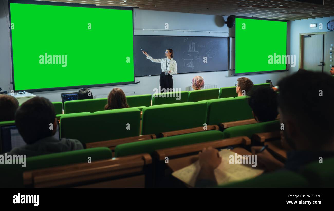 Giovane professoressa universitaria donna che spiega una lezione, puntando su una schermata verde fittizia. Gruppo di diversi studenti multietnici Foto Stock