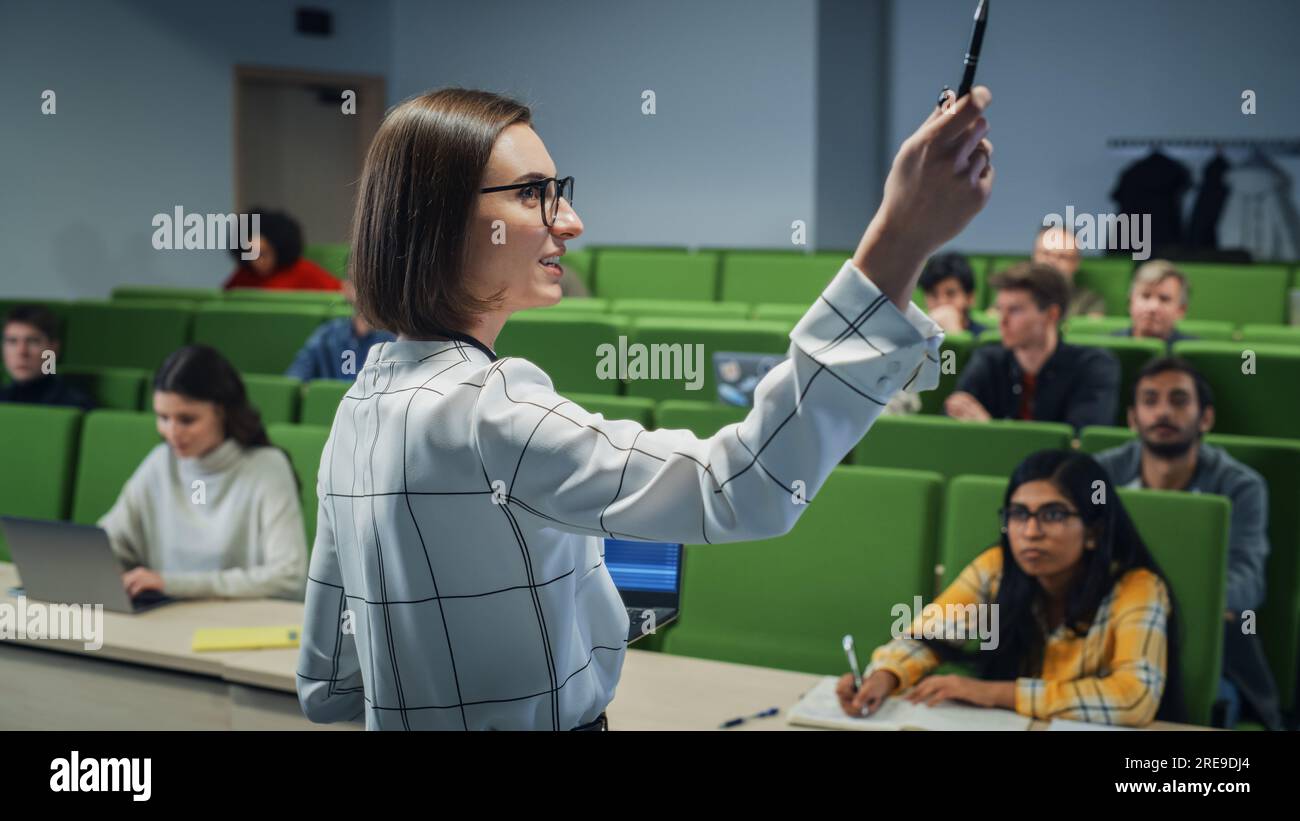 Insegnante che tiene una lezione a un gruppo multietnico eterogeneo di studenti femminili e maschili nella moderna sala del Collegio. Studiosi curiosi e premurosi che studiano Foto Stock