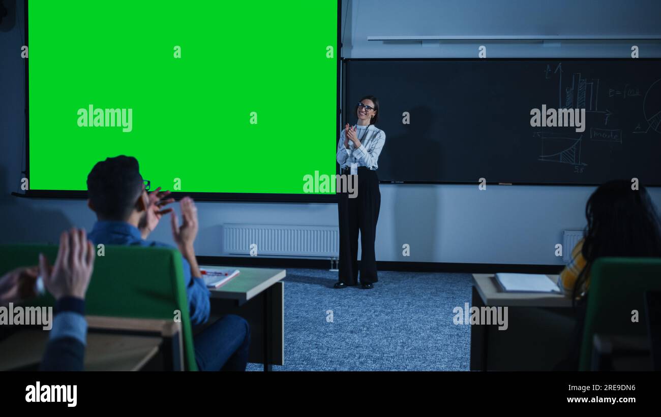 Giovane professoressa universitaria donna che spiega una lezione, puntando su una schermata verde fittizia. Gruppo di diversi studenti multietnici Foto Stock