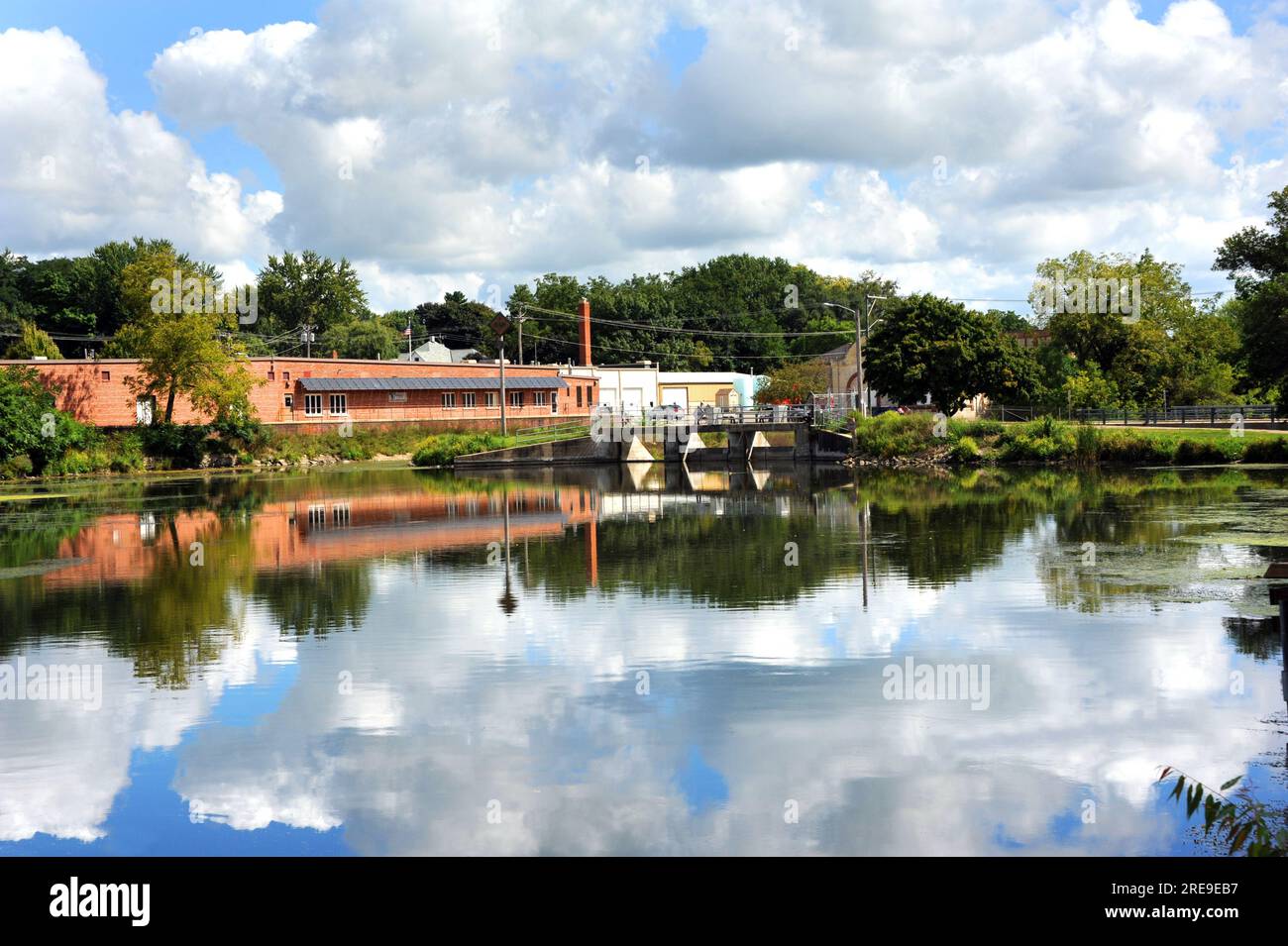 La diga di Stoughton si riflette nelle calme e tranquille acque del fiume Yahara. Questa piccola città del Wisconsin ha edifici, nuvole e cieli blu riflessi Foto Stock