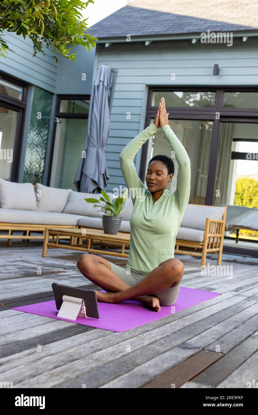 Donna afroamericana che fa yoga, meditando usando un tablet sulla terrazza Foto Stock