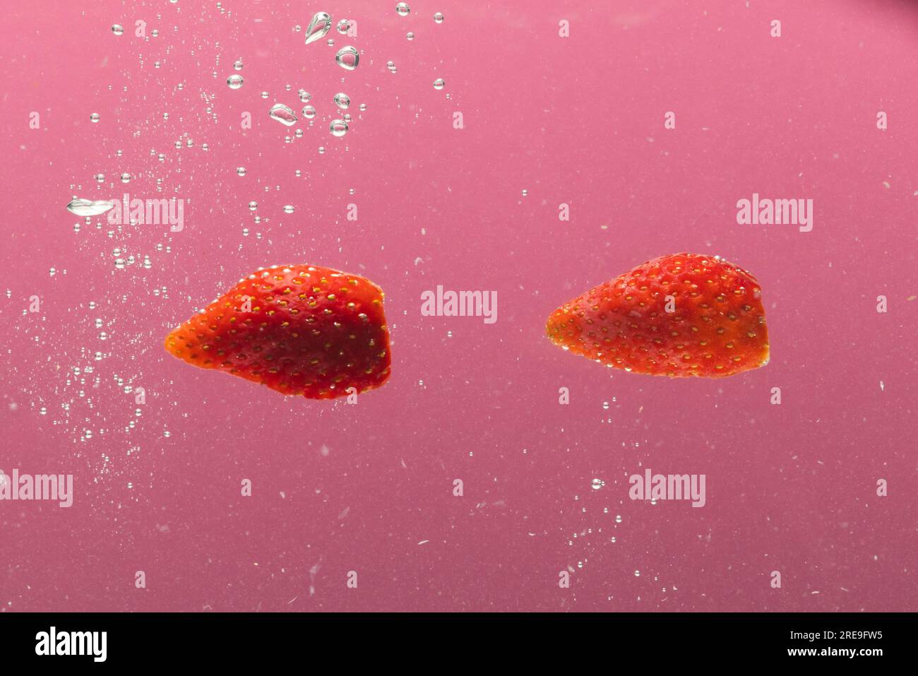Primo piano delle fragole che cadono nell'acqua con spazio per la copia su sfondo rosa Foto Stock