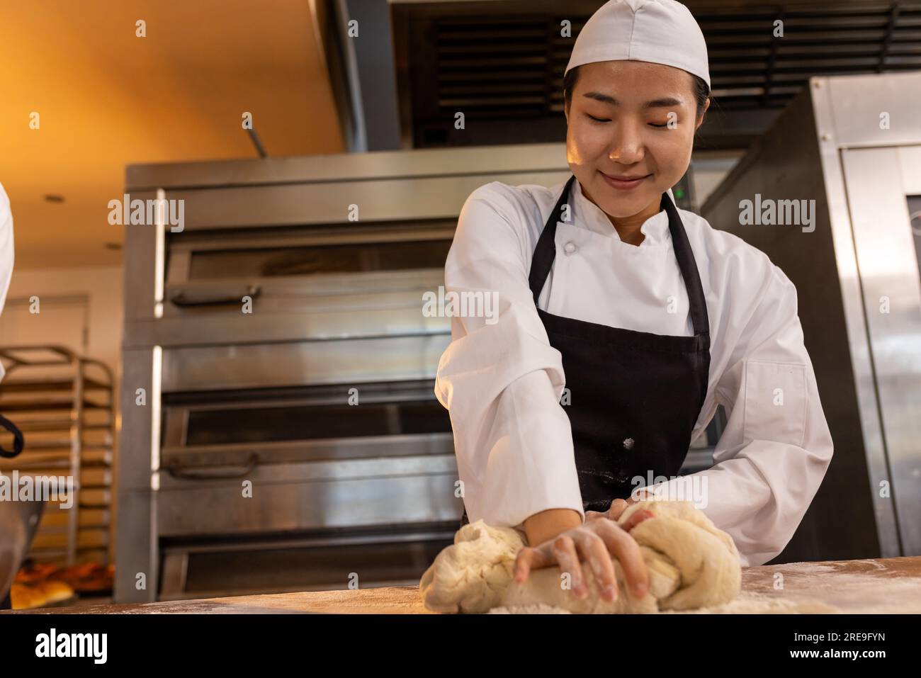 Una bella panettiera asiatica che indossa grembiule nella cucina del panificio e impastare l'impasto Foto Stock