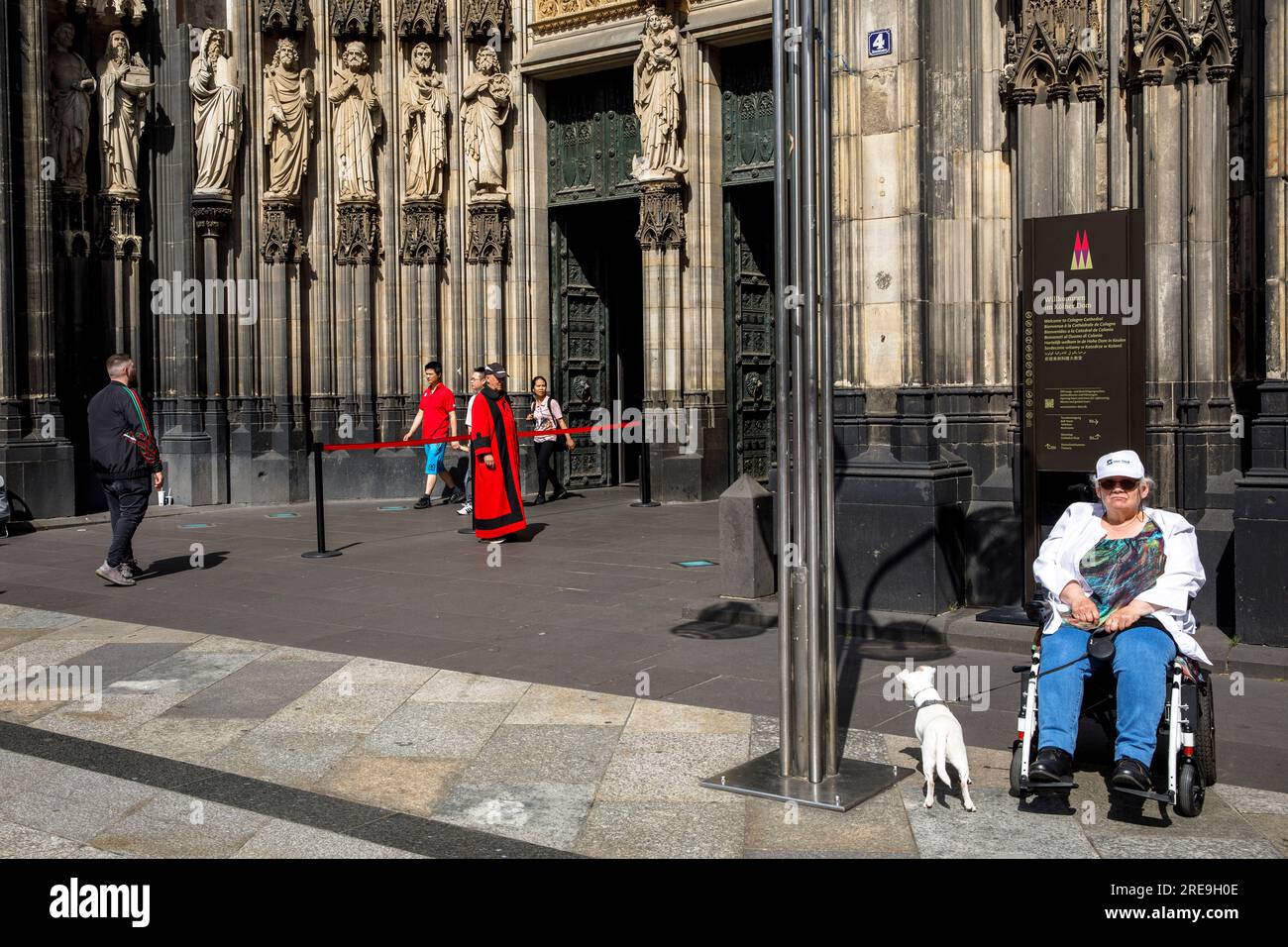 Donna in sedia a rotelle con cane in attesa di fronte al portale della cattedrale, Colonia, Germania. Frau im Rollstuhl mit Hund wartet vor dem Domportal, Koeln, D. Foto Stock