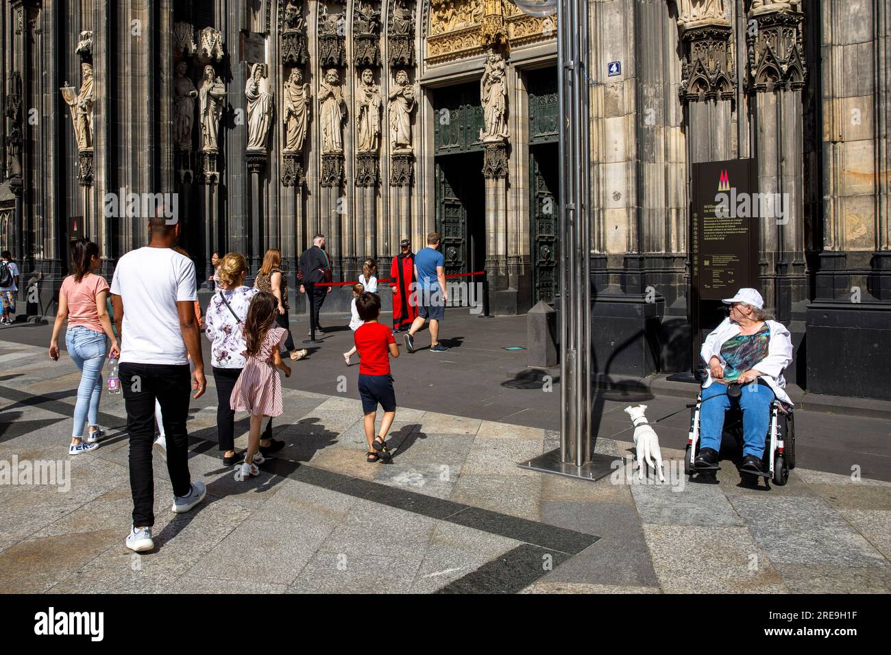 Donna in sedia a rotelle con cane in attesa di fronte al portale della cattedrale, Colonia, Germania. Frau im Rollstuhl mit Hund wartet vor dem Domportal, Koeln, D. Foto Stock