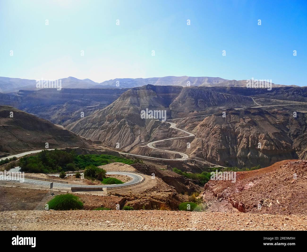 Una strada a serpentina in un paesaggio montano desertico sotto il cielo azzurro Foto Stock