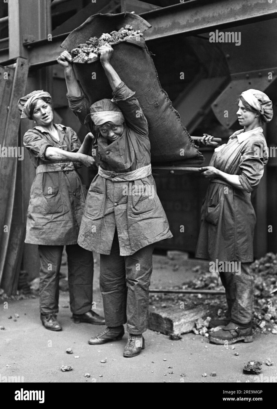 Horace Nicholls - due riempitrici femminili usano due pali corti per aiutare una caldaia femminile mentre solleva un sacco di coca sulla schiena - Foto Stock