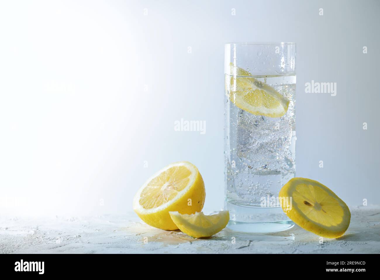 Acqua gassata con cubetti di ghiaccio e limone in un bicchiere, bevanda rinfrescante su sfondo grigio chiaro, spazio copia, messa a fuoco selezionata, narr Foto Stock