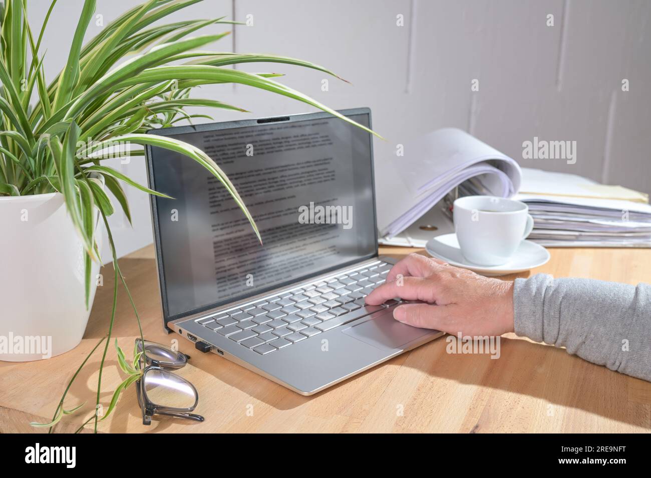 La mano sta scrivendo su un computer portatile, una tazza da caffè, una pianta e una cartella di file su una scrivania in legno, concetto aziendale, spazio di copia, messa a fuoco selezionata, profondità ridotta di f Foto Stock