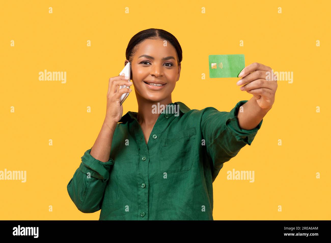 Black Lady che parla sul cellulare con carta di credito, sfondo giallo Foto Stock