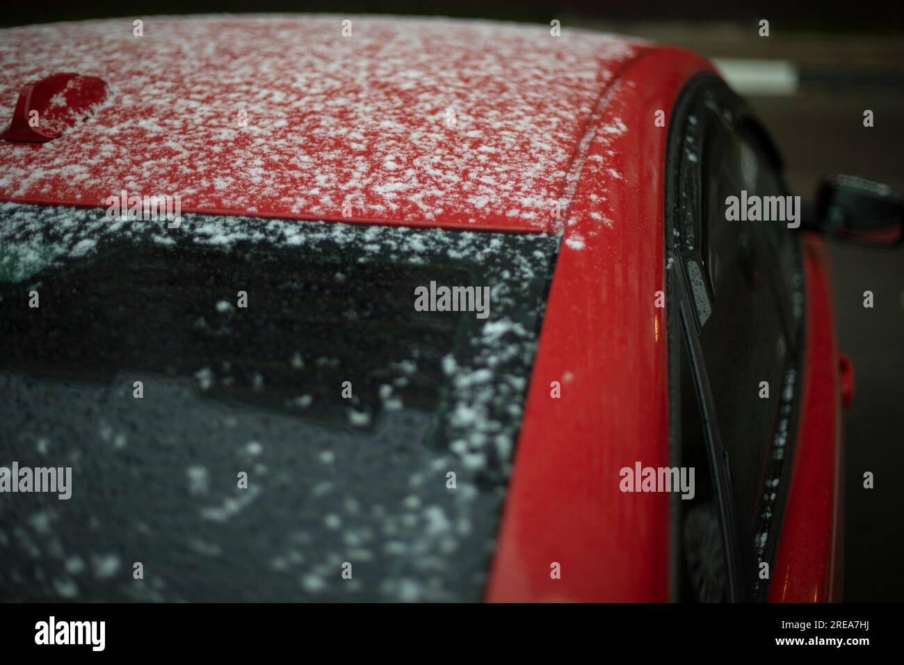 Auto rossa nella neve. Parti della carrozzeria dopo le precipitazioni. L'auto è parcheggiata in inverno. Lunotto di trasporto bagnato. Foto Stock