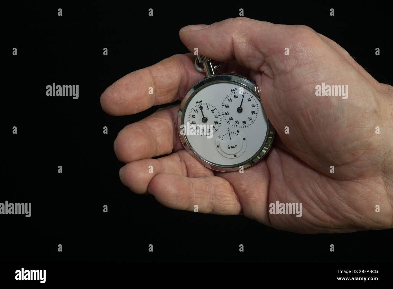 Cronometro, un uomo tiene in mano un cronometro su sfondo nero Foto Stock
