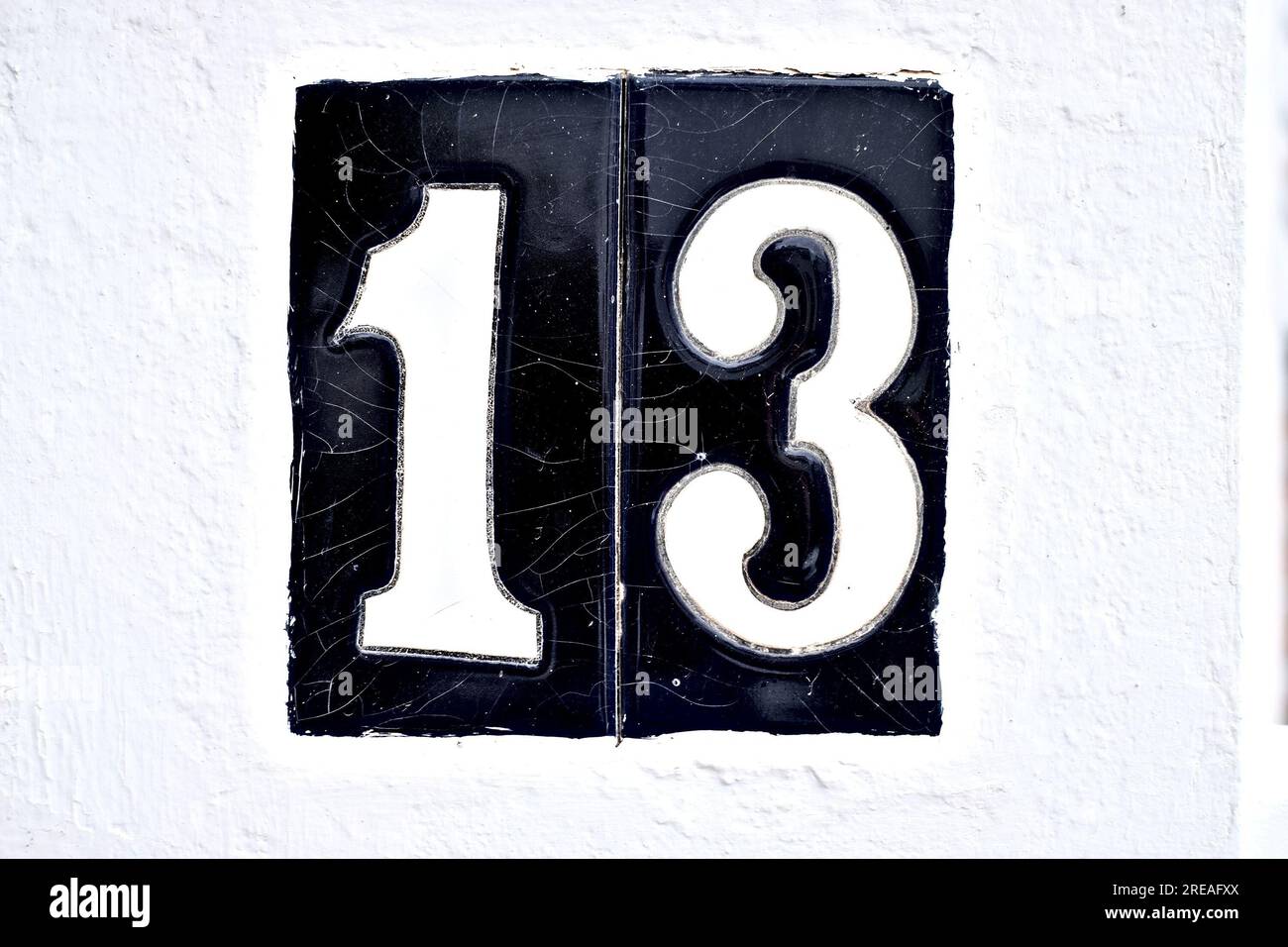 Grande numero 13, tredici, su piastrelle nere su un muro bianco. Foto Stock