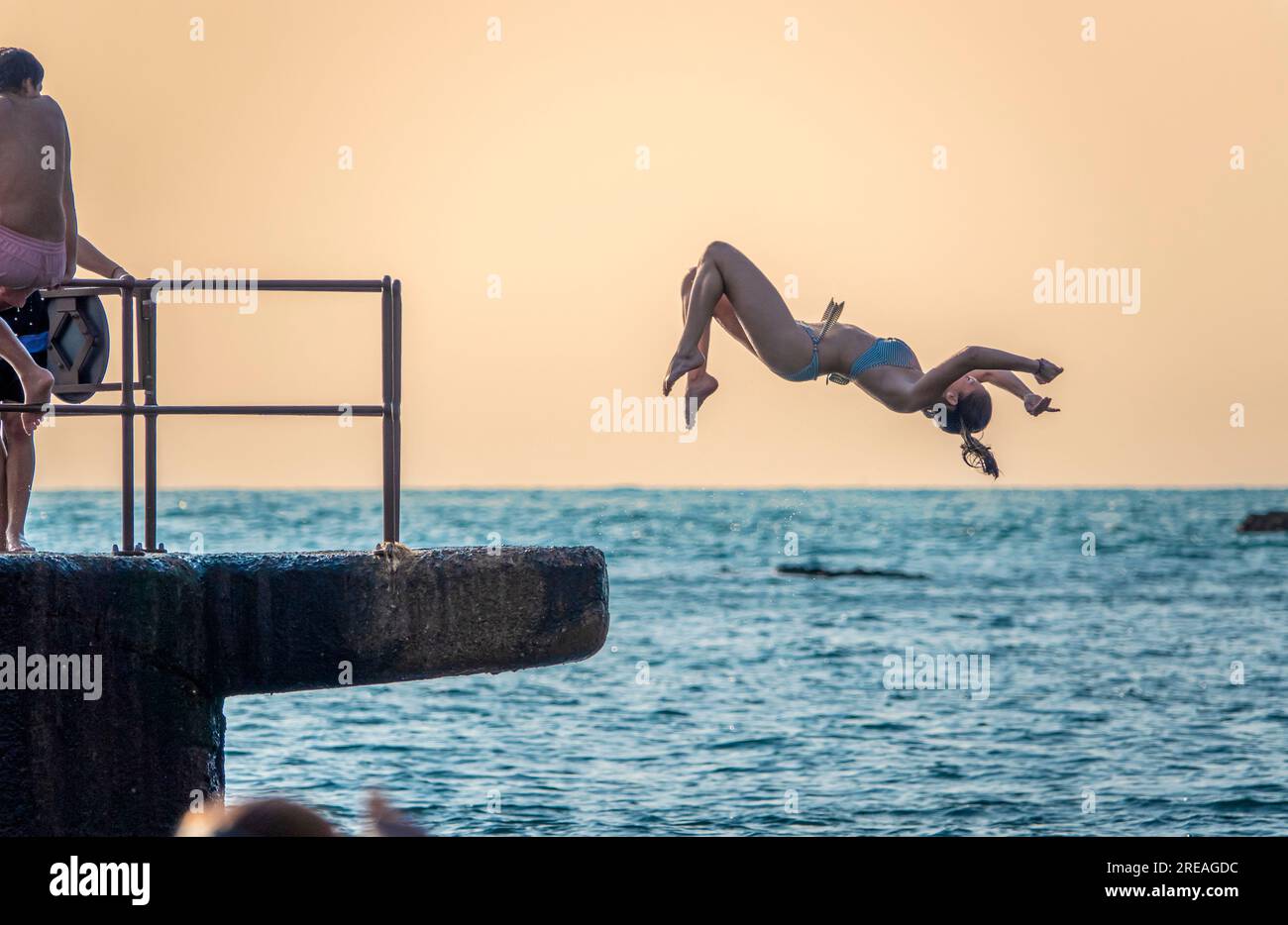 Giovani che saltano in mare al tramonto su una spiaggia in estate. Foto Stock